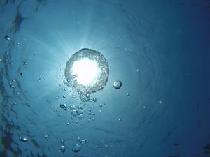 Captivating underwater view of sunlit bubbles rising against a blue ocean background.